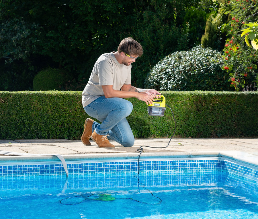Mann kniet am Pool und hält eine RYOBI 18 V One+ Akku-Tauchpumpe ohne Akku und Ladegerät.