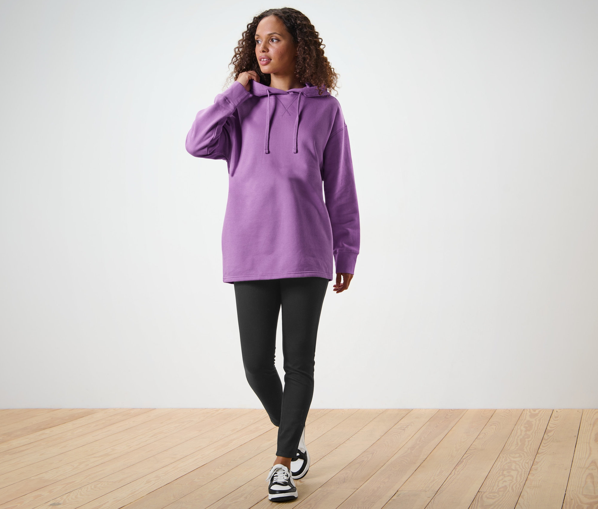 Frau geht und justiert die Kapuze ihres langen Kapuzensweatshirts.