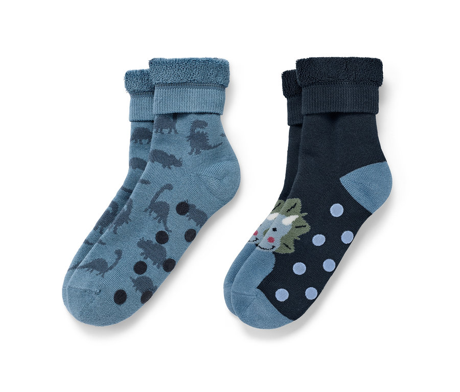 Zwei Paar Kinder-Antirutsch-Socken: Ein Paar blau mit Dinosauriern und braunen Punkten, das andere dunkelblau mit Dinosaurier-Motiv und blauen Punkten.