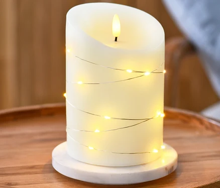 Eine LED-Echtwachskerze mit Microlichterkette steht auf einem runden Holztisch.