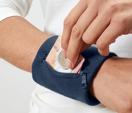Eine Hand legt einen Euroschein und eine Münze in eine blaue Sicherheits-Geldbörse für das Handgelenk.