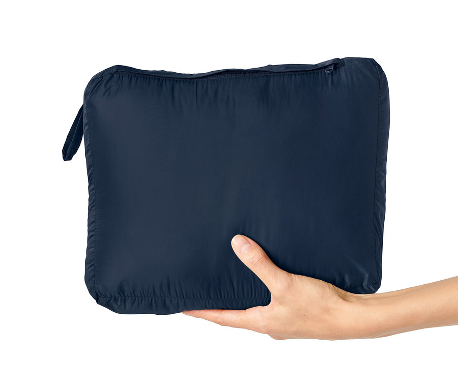 Eine Hand hält eine ultraleichte Reisedecke in einer marineblauen Verpackung.
