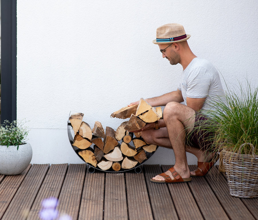 Mann mit Hut legt Holz in ein Cook King Kaminholzregal.