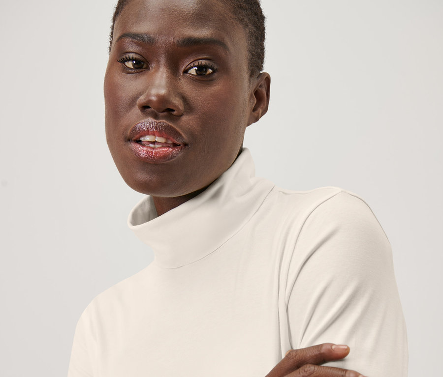 Porträt einer Frau, die ein cremeweißes Rollkragenshirt trägt.