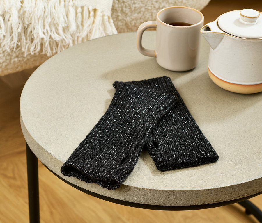 Auf einem Tisch liegen glitzernde Strick-Handstulpen neben einer Tasse und einer Teekanne.