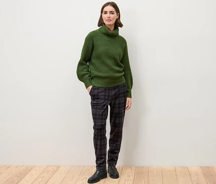 Eine Frau steht in einem grünen Pullover und einer karierten Joggpants.