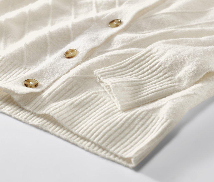 Detailansicht eines cremeweißen Cardigans mit Strickstruktur.