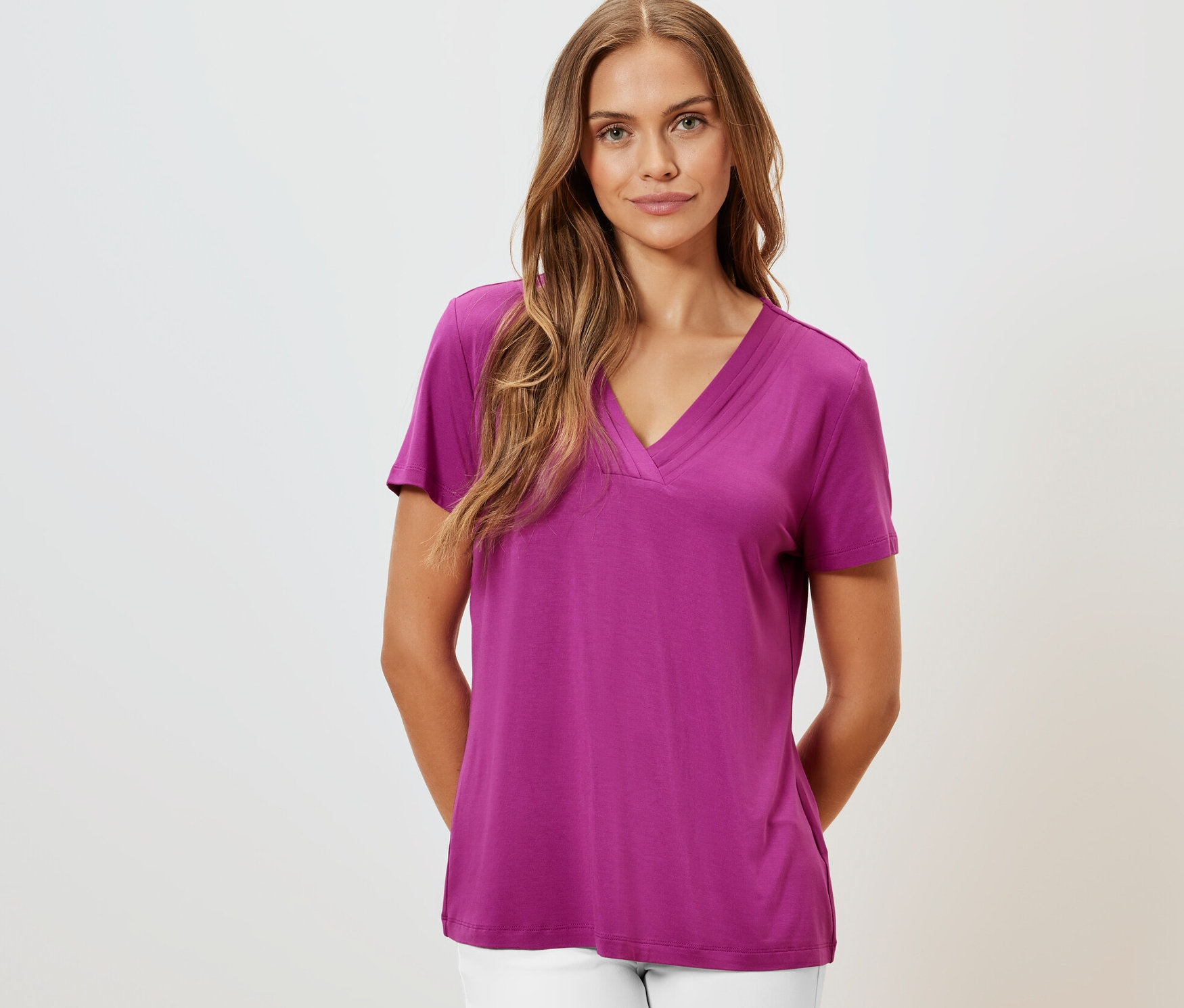 Frau trägt ein Shirt mit Faltendetail in Berry-Farbe und weiße Hose.