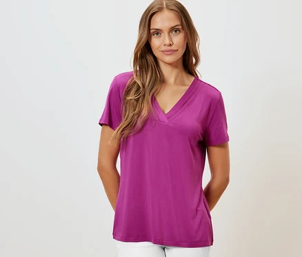 Frau trägt ein Shirt mit Faltendetail in Berry-Farbe und weiße Hose.