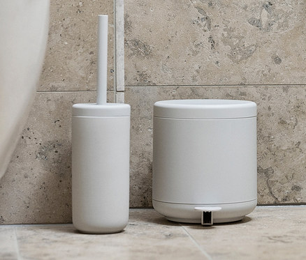 Im Badezimmer stehen neben der Toilette ein hellgrauer ZONE DENMARK Pedaleimer »Ume« und eine Toilettenbürstenhalterung. An der Wand hängen ein weißes Handtuch und in einem Blumentopf steht eine Pflanze.
