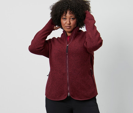 Frau richtet ihre Haare, trägt eine dunkelrote Strickfleece-Jacke und Thermo-Jazzpants.