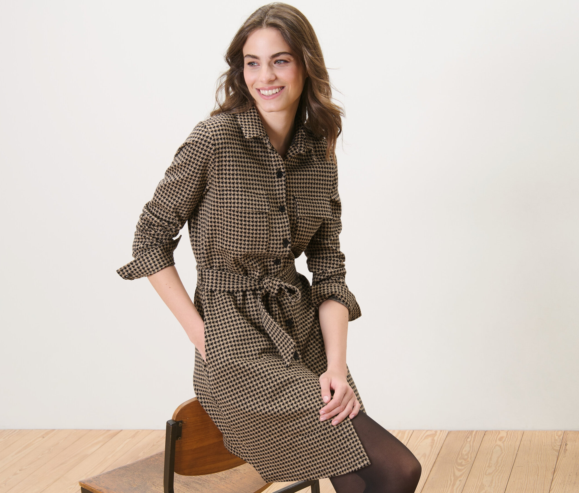 Frau sitzt auf einem Stuhl und trägt ein Sweatkleid mit Hahnentritt-Jacquard.