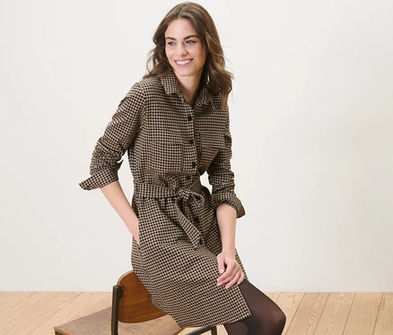 Frau sitzt auf einem Stuhl und trägt ein Sweatkleid mit Hahnentritt-Jacquard.