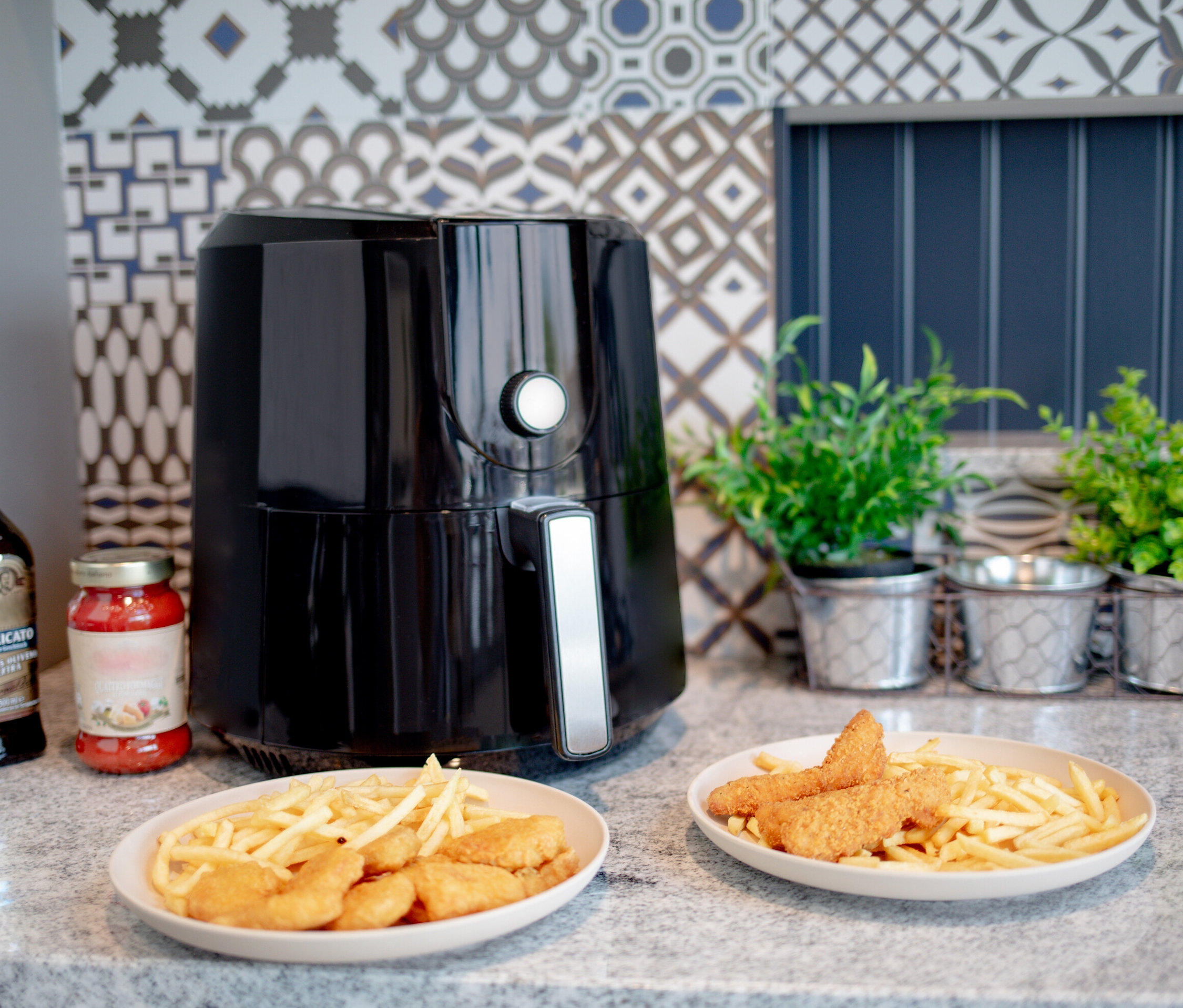 Auf einer Küchentheke steht eine schwarze Steba Heißluftfritteuse HF 5000 neben zwei Tellern mit Pommes und Chicken Nuggets.