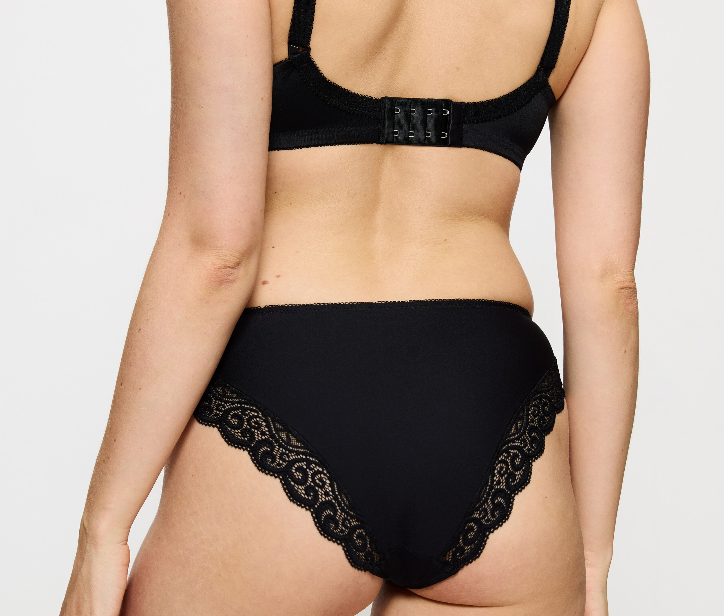 Rückansicht einer Frau, die einen schwarzen BH und einen Triumph Amourette Tai Slip trägt.