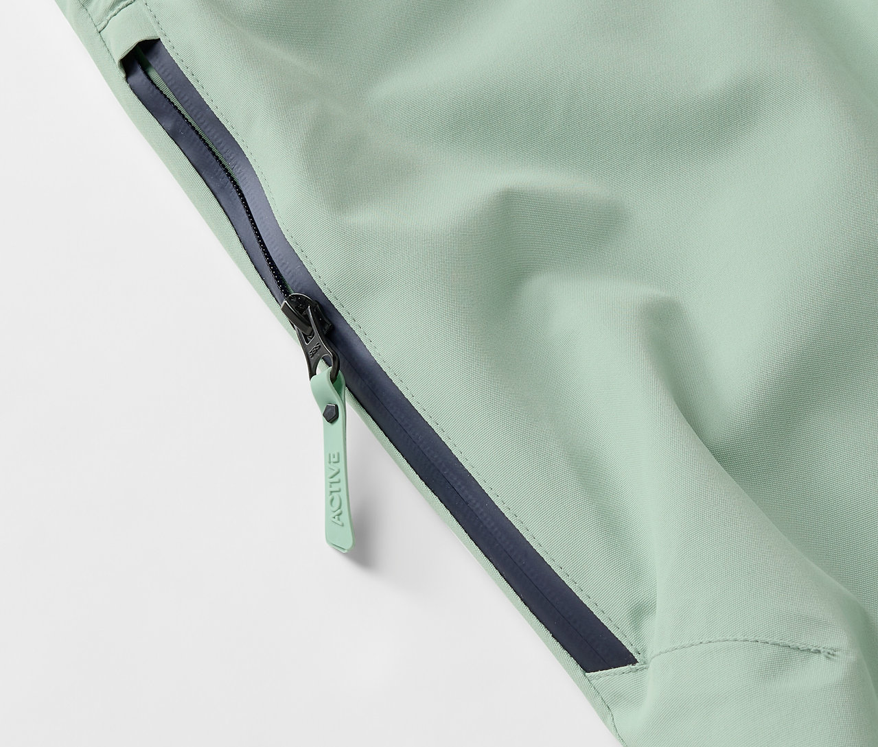 Detailaufnahme einer hellgrünen Jacke mit Reißverschluss und dunkelblauem Saum.