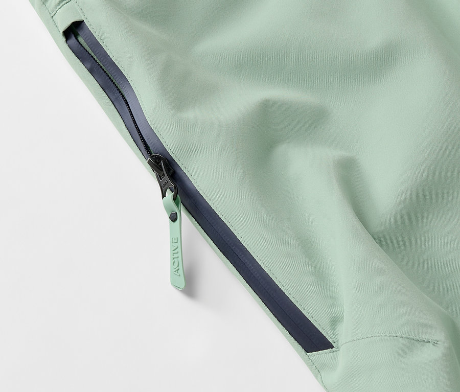 Detailaufnahme einer hellgrünen Jacke mit Reißverschluss und dunkelblauem Saum.