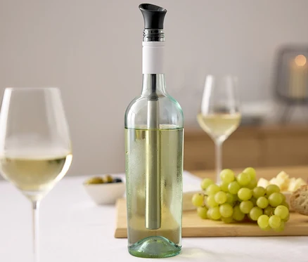Weinflasche mit Wein-Kühlstab, zwei Gläser Wein, Trauben, Käse und Brot auf einem Tisch.