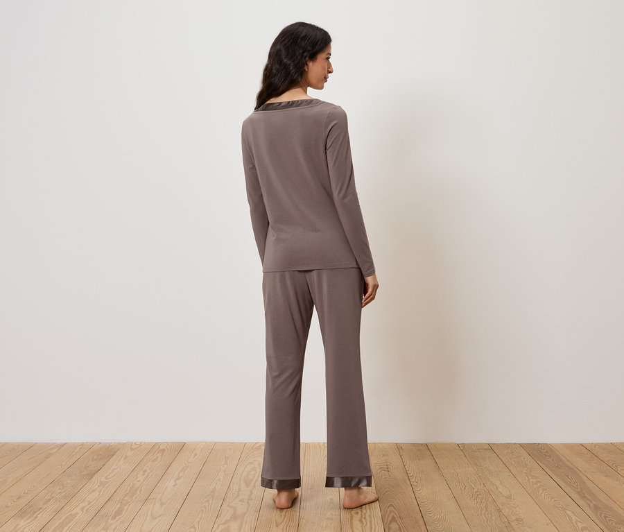 Frau im braunen Pyjama steht mit dem Rücken zur Kamera.