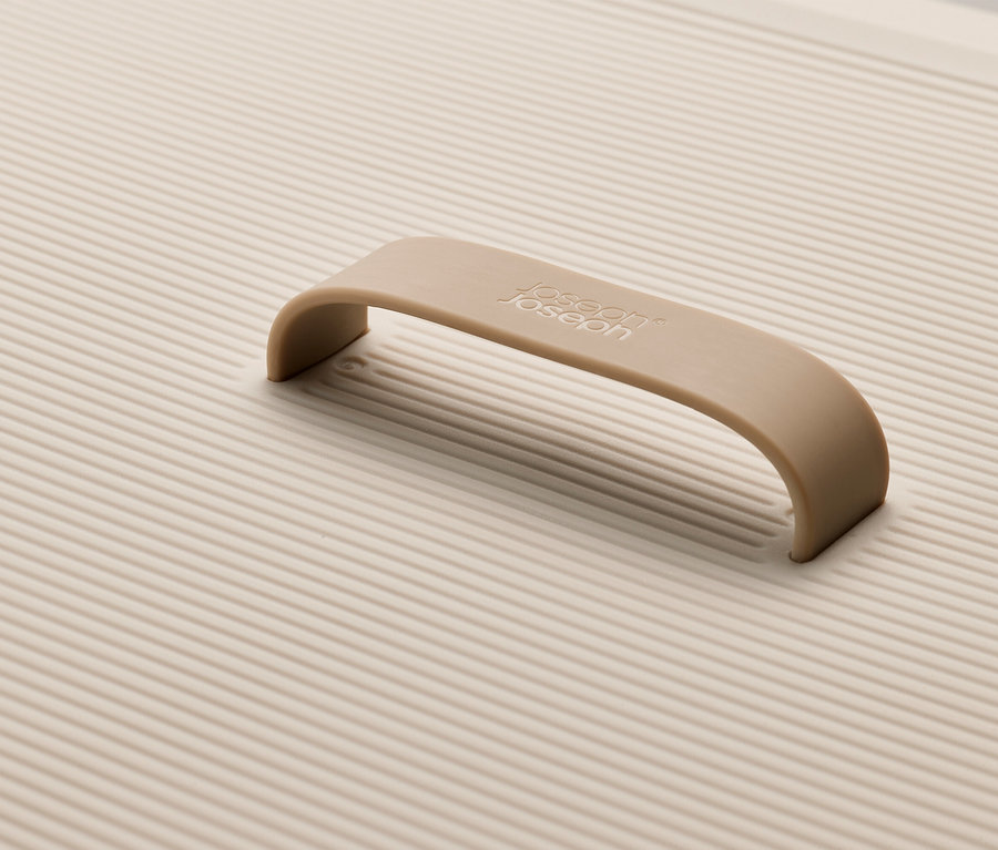 Detailaufnahme eines cremefarbenen Joseph Joseph Schneidebretts mit geriffelter Oberfläche und Griff.