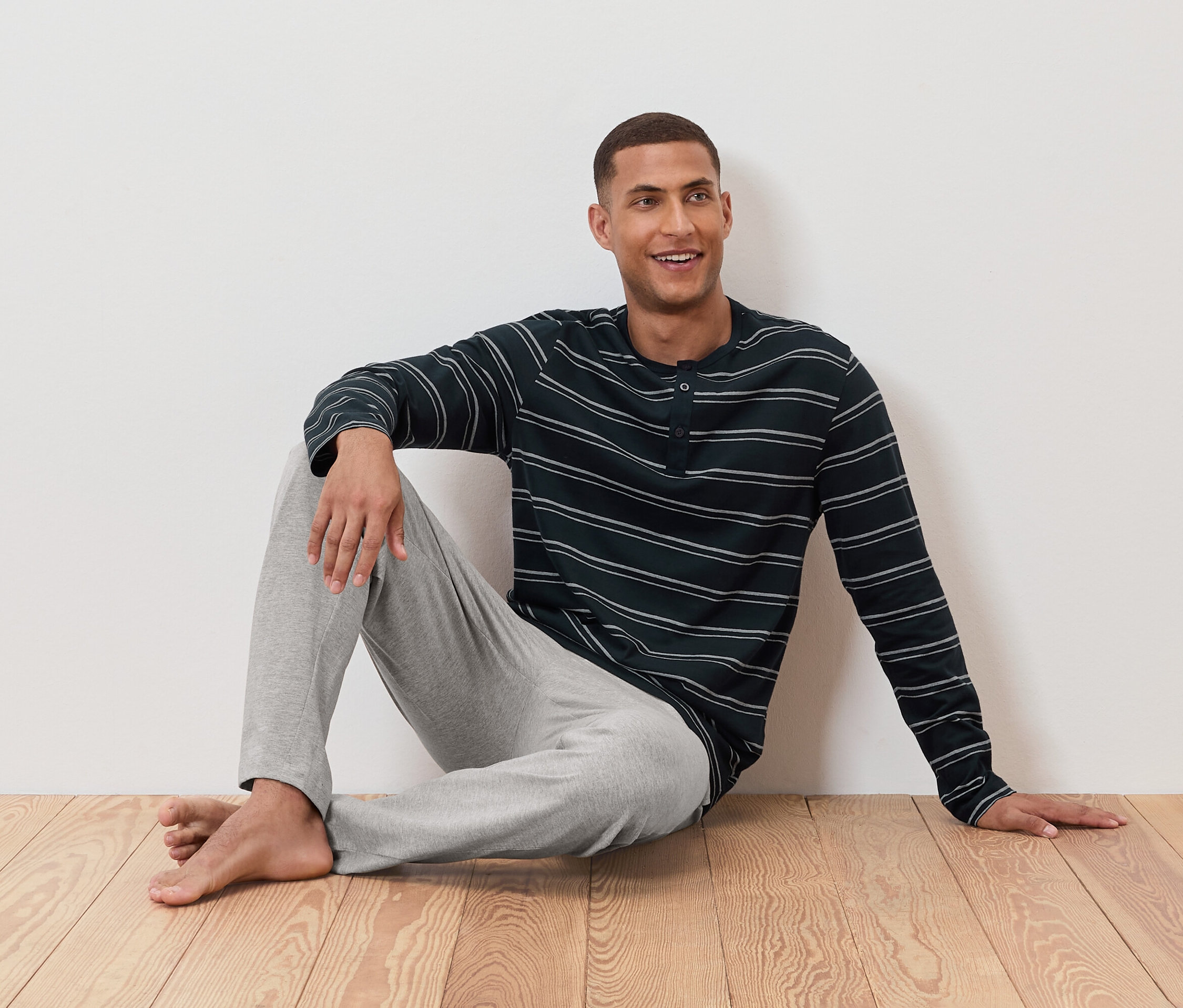 Mann sitzt im gestreiften Schlafanzugoberteil und grauer Hose am Boden.