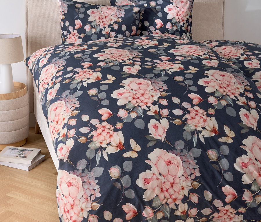 Ein Bett mit blumiger Bettwäsche und einem Nachttisch mit Lampe.