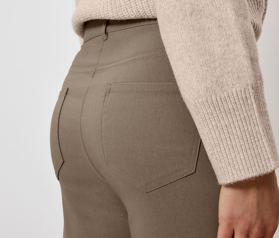 Detailaufnahme einer Frau, die eine braune Hose und einen beigen Pullover trägt.