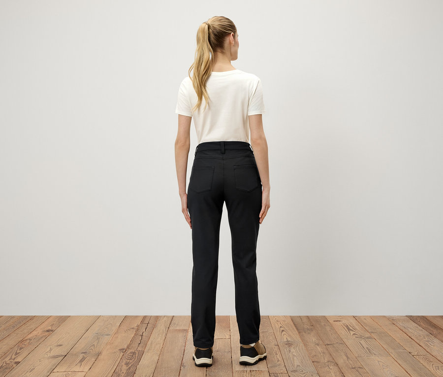 Rückansicht einer Frau mit blonden Haaren, die zu einem Pferdeschwanz gebunden sind, trägt ein weißes T-Shirt und eine schwarze Hose.