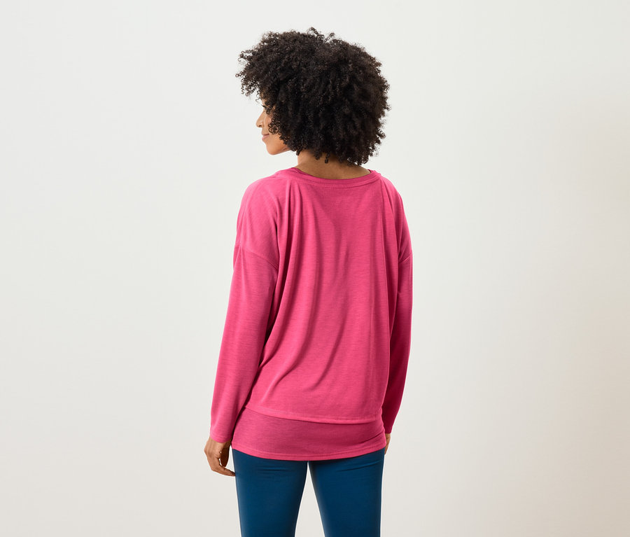 Von hinten ist eine Frau mit Afro-Frisur in einem rosa Pullover und blauen Hosen zu sehen.