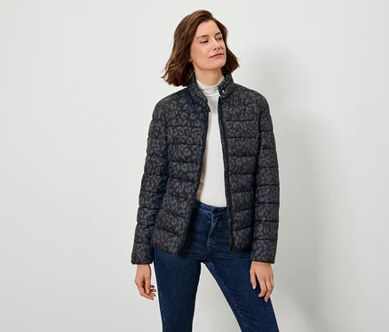 Frau trägt eine schwarze Daunenjacke mit Muster und Jeans.