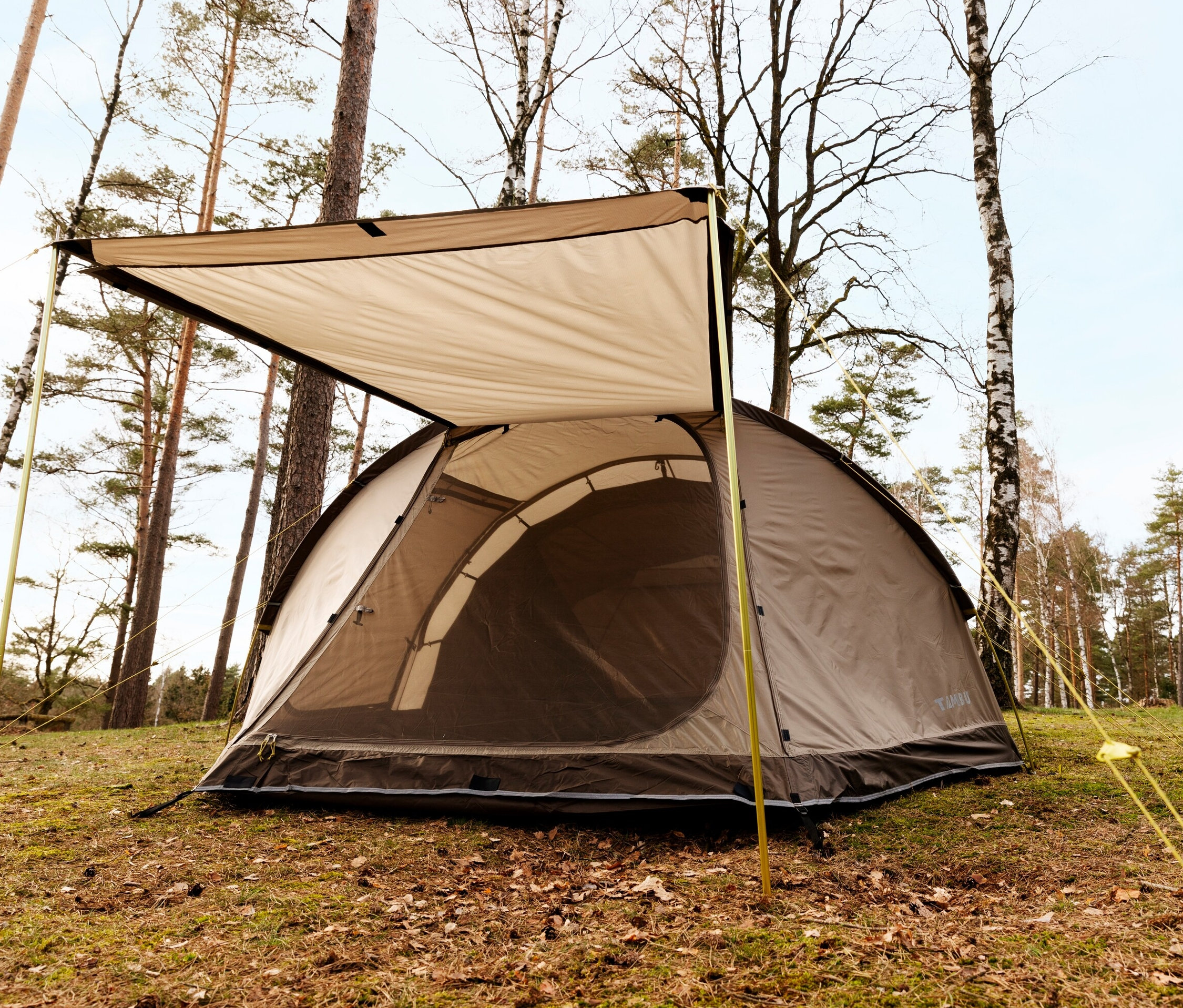 Ein braunes Tambu 4-Personen-Tunnelzelt »DURDANTA 4« steht auf einer Wiese zwischen Bäumen.