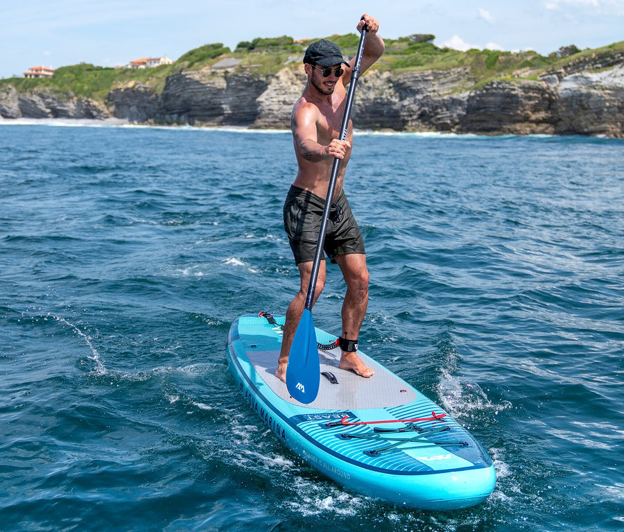 Ein Mann paddelt auf einem blauen Aqua Marina SUP Board »Beast« 10'6" auf dem Meer.