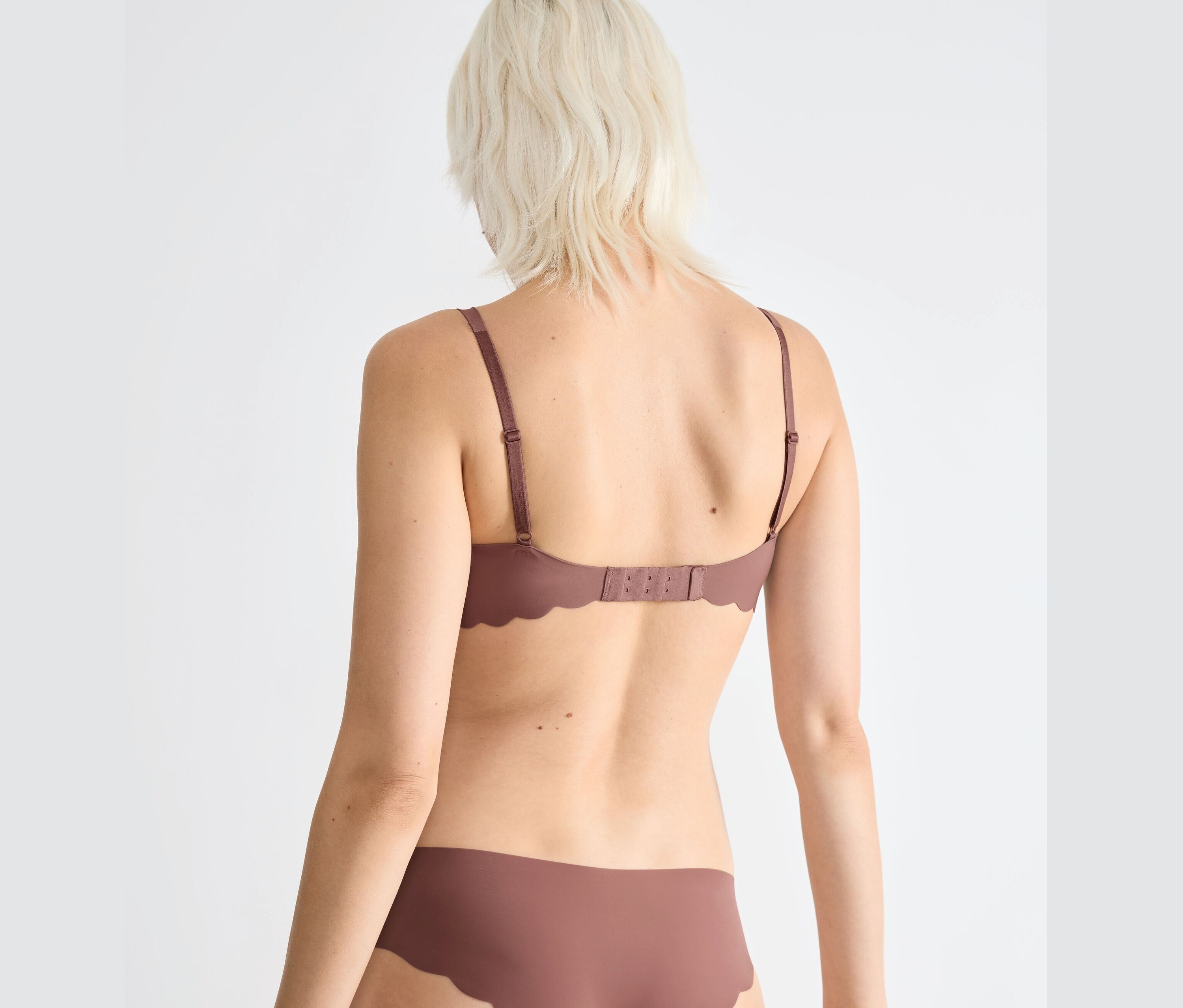 Rückansicht einer blonden Frau, die einen braunen sloggi ZERO Microfibre 2.0 Soft BH und Slip trägt.