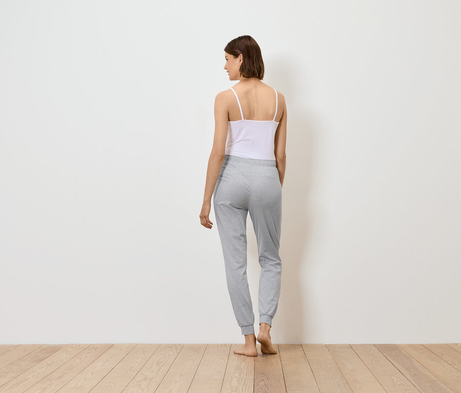 Frau steht mit dem Rücken zum Betrachter, trägt ein weißes Top und graue Jogginghose.