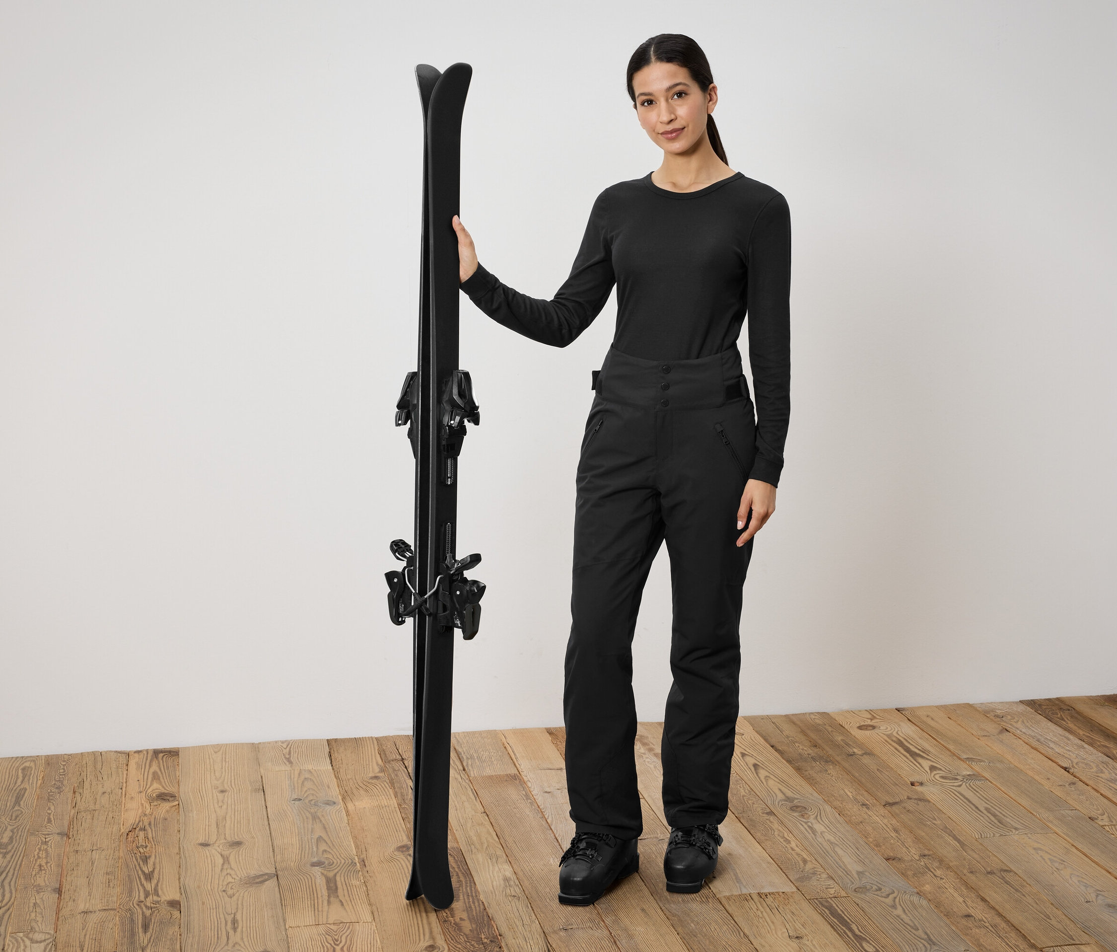 Frau in schwarzer Skibekleidung hält schwarze Ski.