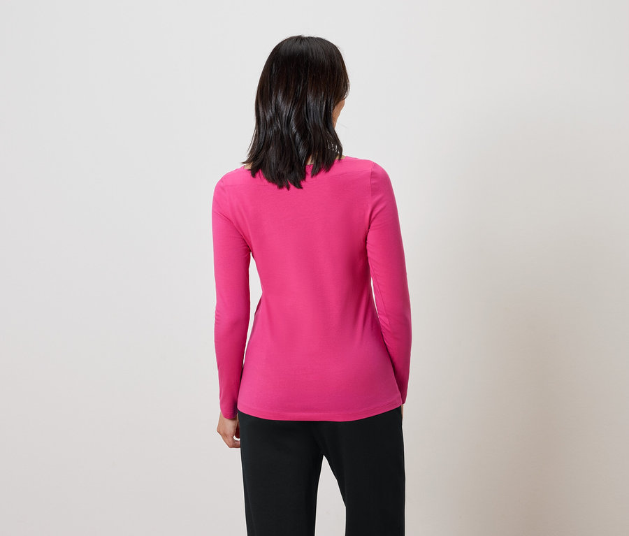 Rückansicht einer Frau mit dunklem Haar in einem pinkfarbenen Pullover und schwarzer Hose.