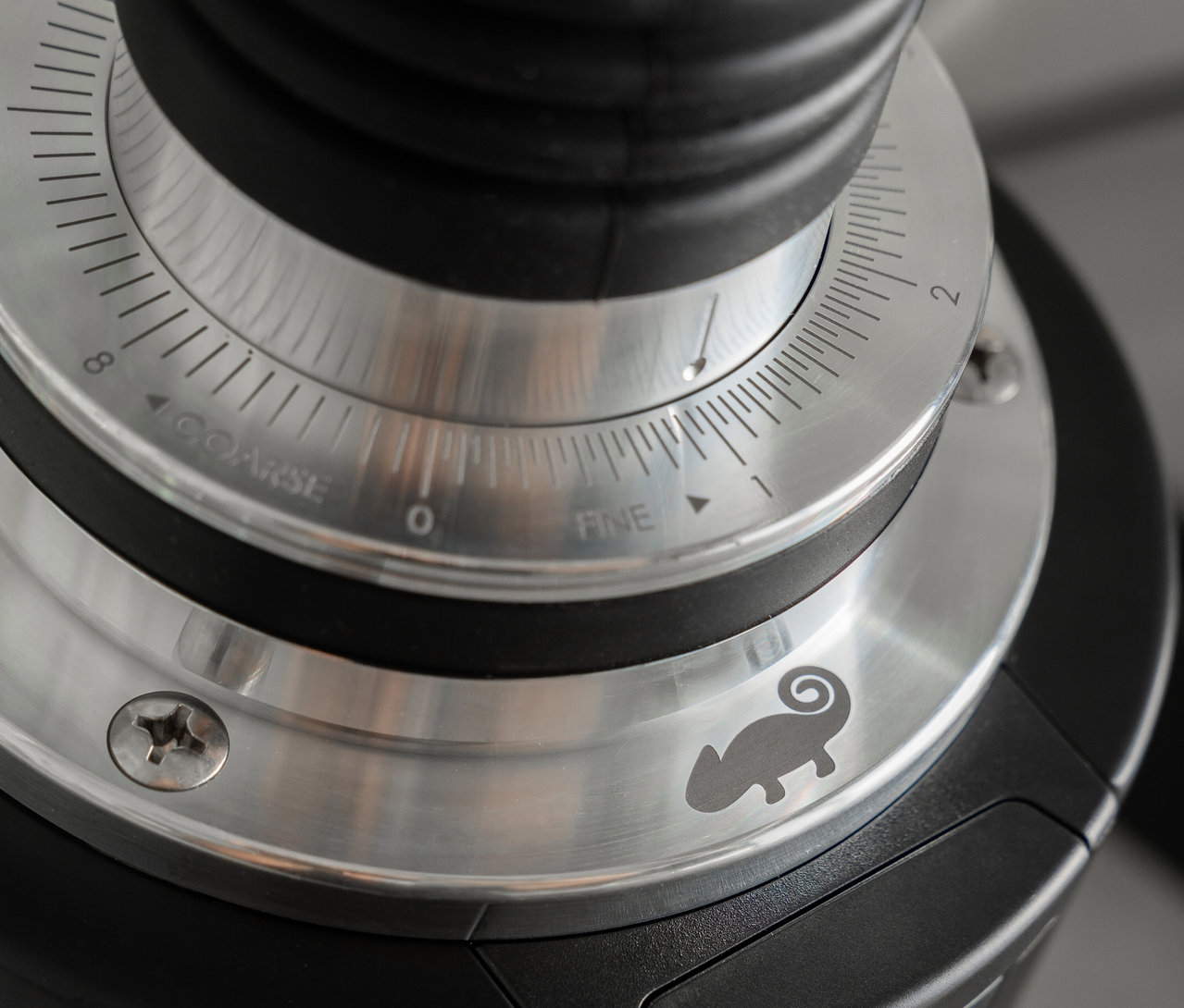 Nahaufnahme einer Kaffeemühle mit Fokus auf den Einstellring, der von 'Fein' zu 'Grob' justiert werden kann. Ein Chamäleon-Logo ist sichtbar.