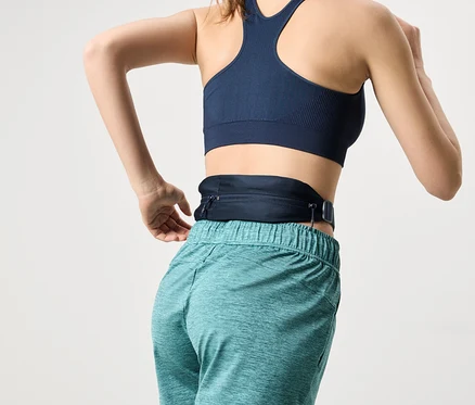 Frau von hinten, die einen marineblauen Sport-BH und türkisfarbene Shorts trägt, mit einer marineblauen Gürteltasche um die Taille.
