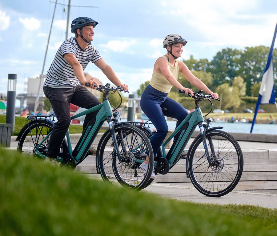 Ein Mann und eine Frau fahren mit Fischer Trekking E-Bikes VIATOR 2.1 ACTIVE, 50 cm vor einer Uferpromenade entlang.