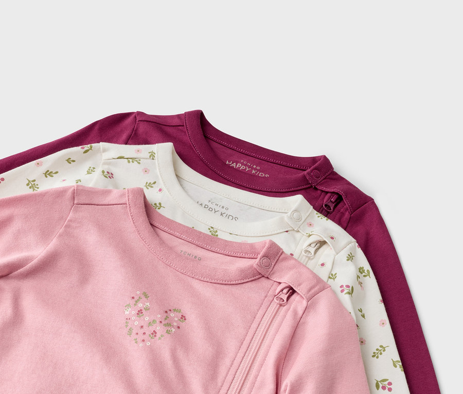 Nahaufnahme von drei Baby-Langarmshirts in Rosa mit Herz, Weiß mit Blumenmuster und Lila mit Reißverschluss.