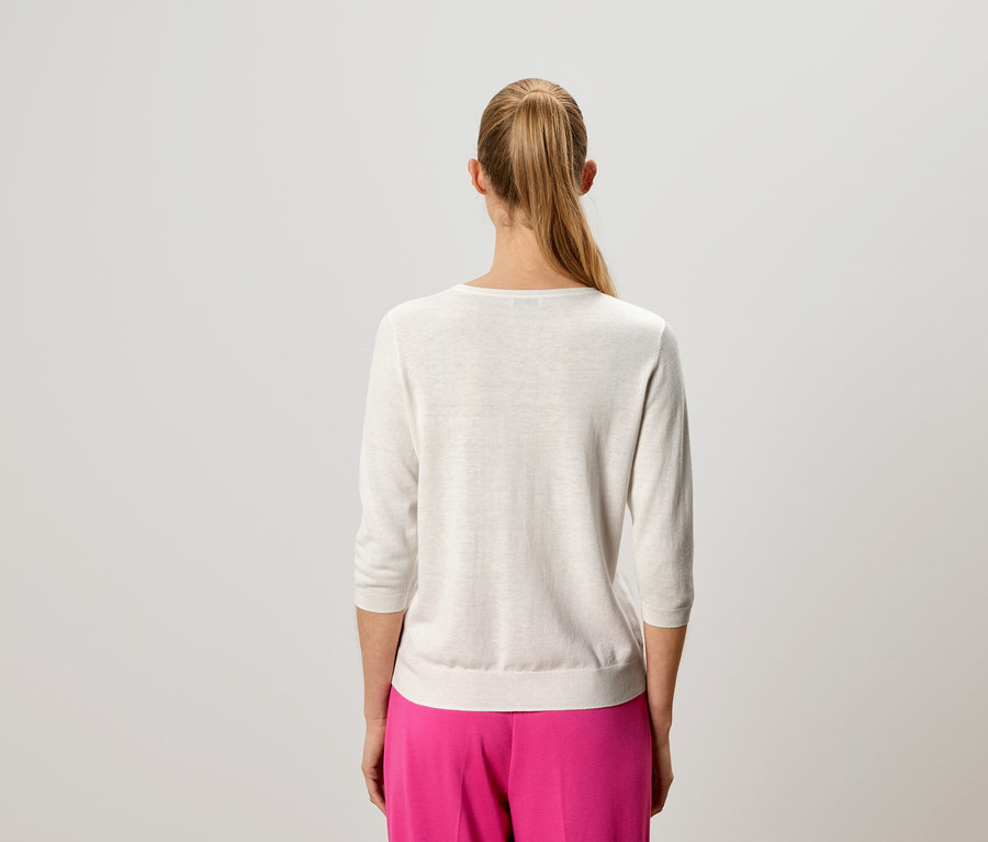 Rückansicht einer Frau mit blondem Haar, die einen hellen Pullover und eine pinke Hose trägt.
