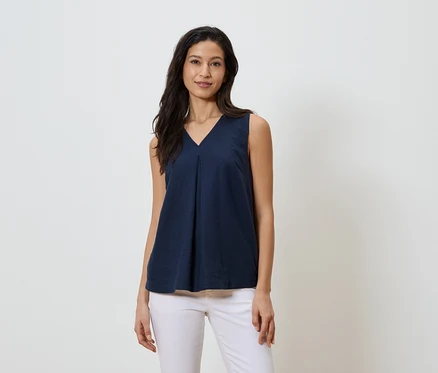Frau trägt ein marineblaues, ärmelloses V-Ausschnitt-Top und weiße Jeans.