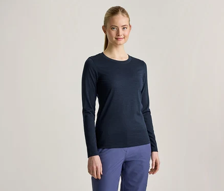 Eine junge Frau mit blondem Pferdeschwanz trägt ein dunkelblaues Langarmshirt und blaue Hosen, sie lächelt in die Kamera.