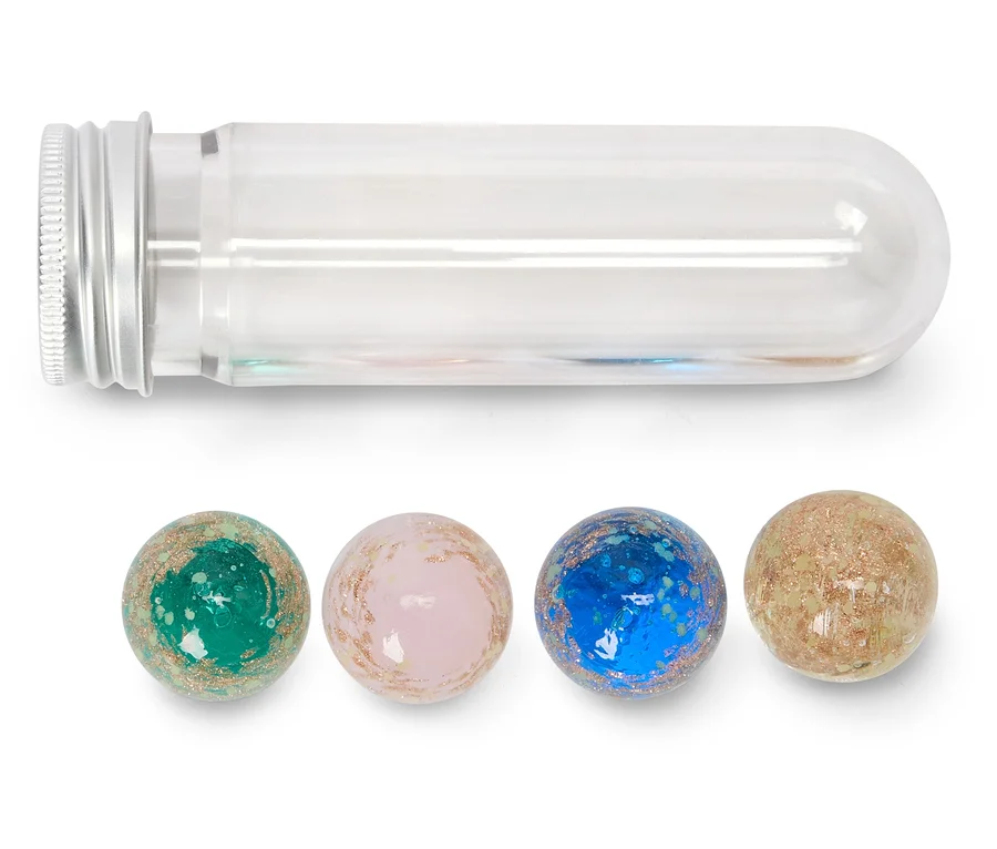 Ein klares Reagenzglas mit silbernem Schraubverschluss liegt horizontal über vier gesprenkelten, glitzernden Kugeln. Die Kugeln sind grün, rosa, blau und beige und liegen in einer Reihe unter dem Glas.