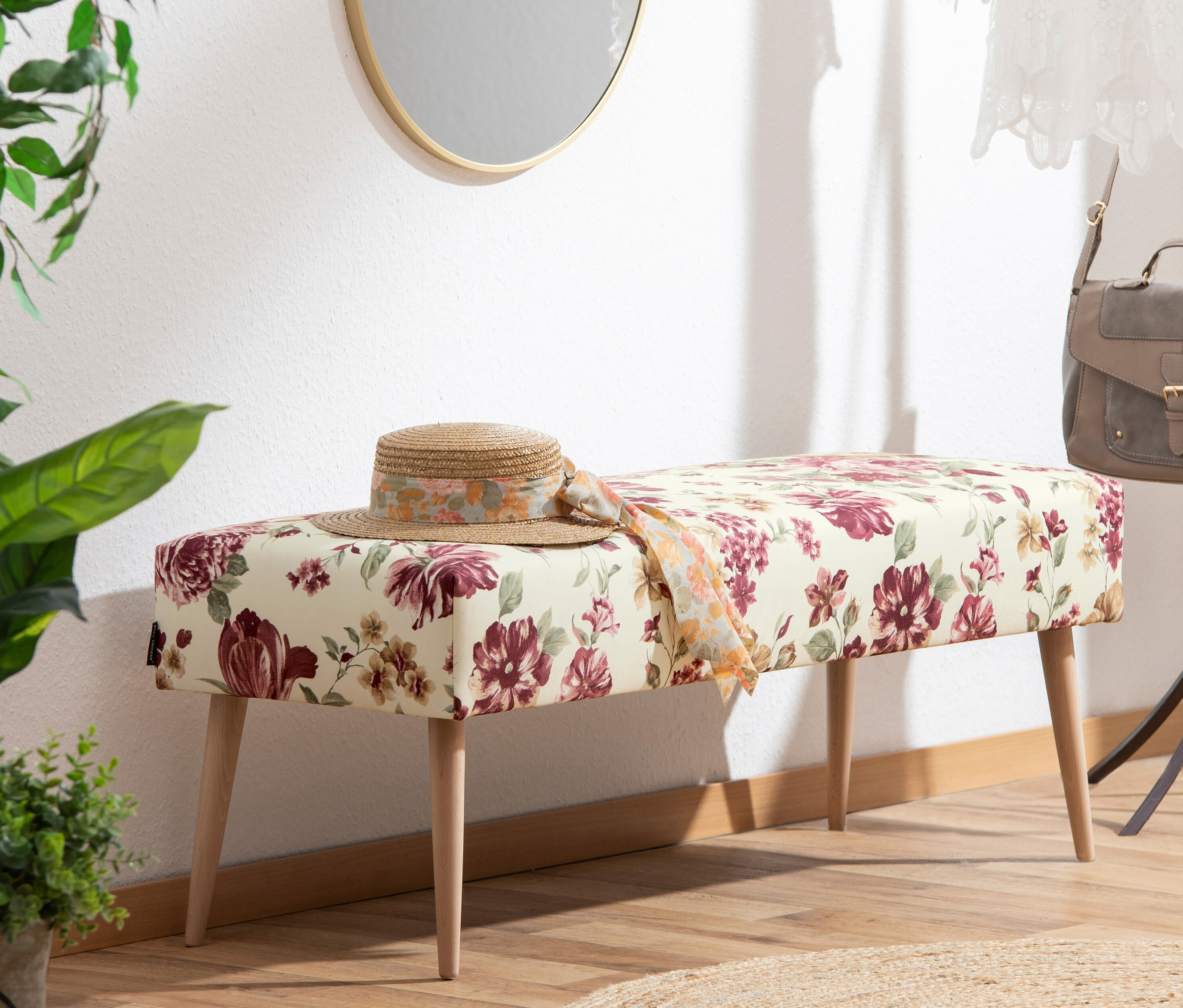 Eine floral beige Sitzbank »Sit« mit einem Hut darauf steht in einem Raum.