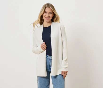 Blonde Frau trägt eine offene, weiße Strickjacke über einem marineblauen T-Shirt und blauen Jeans.