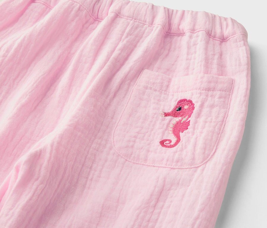 Nahaufnahme einer rosa Hose mit elastischem Bund und einer aufgesetzten Tasche mit einer gestickten Seepferdchenapplikation.