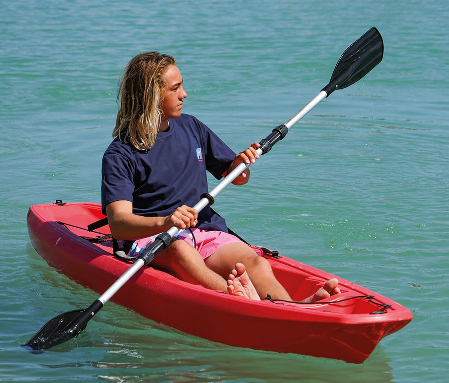Ein Mann mit blonden Haaren paddelt in einem roten Kajak auf dem Wasser.