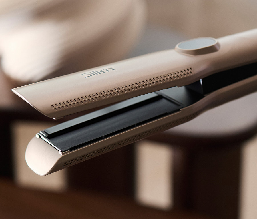 Nahaufnahme eines offenen Silk'n-Haarglätters in Goldbraun, der auf einem Tisch liegt.