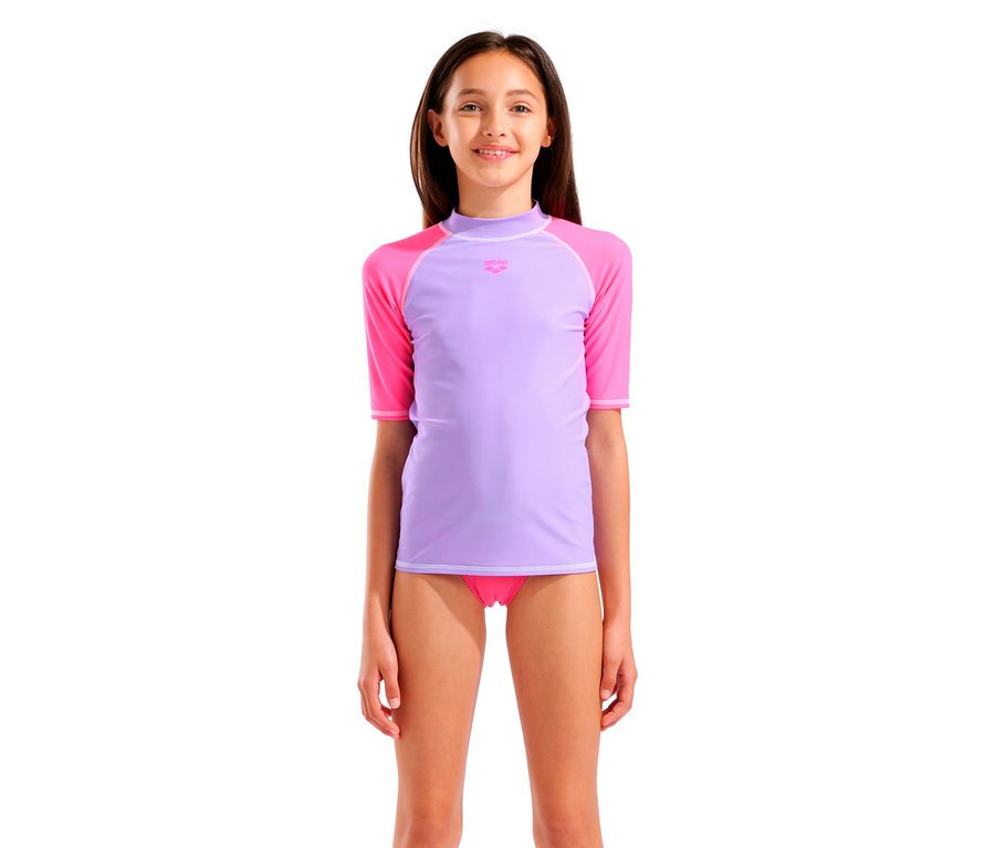 Mädchen mit lila und pinkfarbenem Arena-Badeoberteil und pinkfarbener Badehose, vor einem weißen Hintergrund.